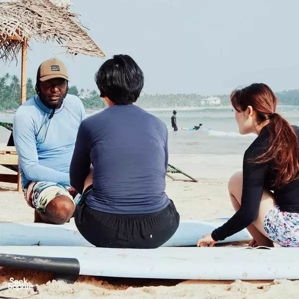 Freedom Surf Sri Lanka instructor seated beside students on Weligama beach, warming up with surfboards laid on the sand