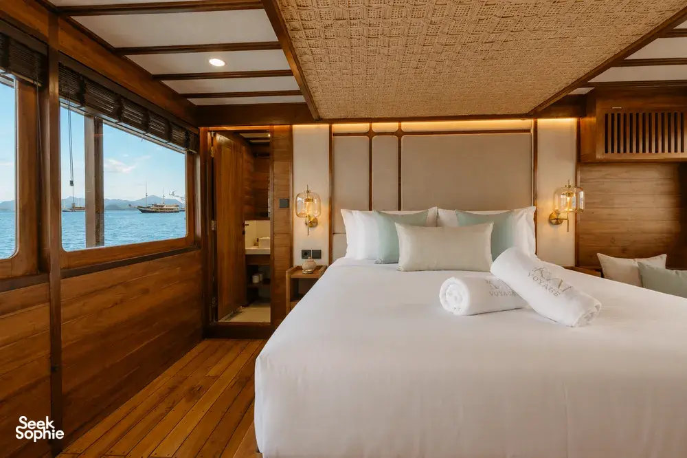 Travass Life new phinisi double cabin with a made bed, warm lighting and an ocean view through the window on a Komodo Island trip