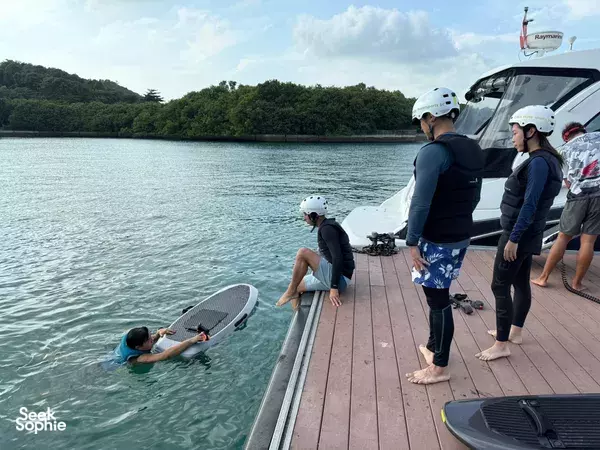 Helmets and wetsuits on as travellers prepare for efoil and jetboard from a Singapore yacht, with one rider practising in the water