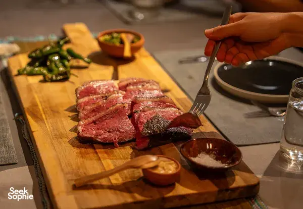 Sliced grilled beef on a wooden carving board with dipping sauces, while a hand carves and serves at private dining Singapore
