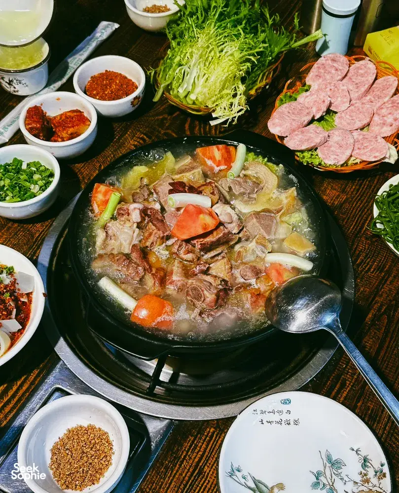 Hotpot tabletop in Lijiang with a bubbling central pot, sliced meats, shredded cabbage, and small bowls of chilli seasoning