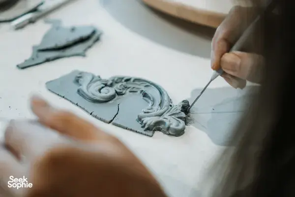 Hands carving an antique-style ceramic plate ornament with a needle tool at Ina Atelier pottery workshops in Singapore