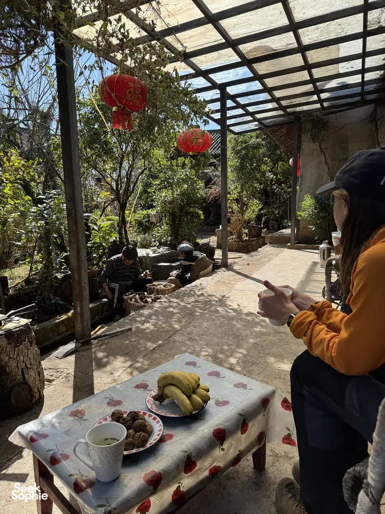 Traveller seated at a table in a Lijiang guesthouse courtyard, with fruit in the foreground and a covered terrace behind