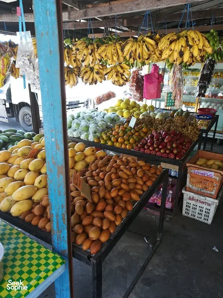 Close view of a Langkawi fruit and produce stall with bananas overhead and stacked oranges and other tropical fruits on counters