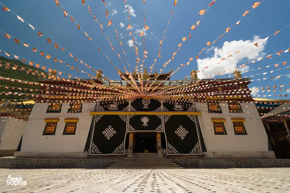 Tibetan temple courtyard in Shangri-La with an ornate entrance and colourful prayer flags overhead, on the cultural part of the 6-day loop
