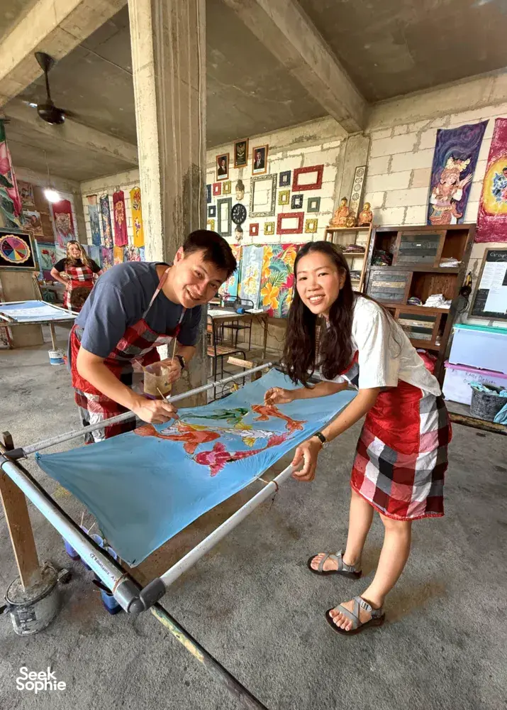 Batik workshop at Five Arts Studio in Keliki, two people paint colourful motifs on fabric stretched on a batik frame in Ubud
