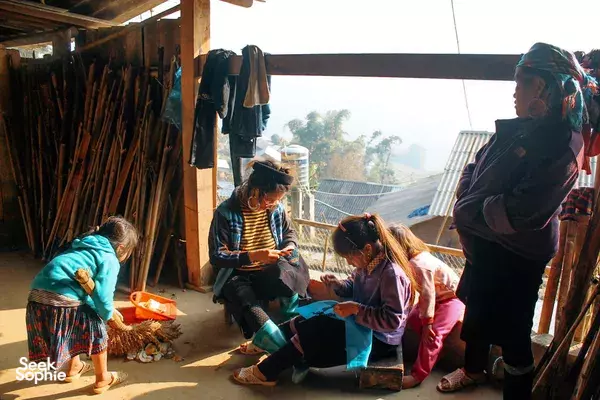 People seated in a village workshop, collaborating over colourful textile crafts at a wooden shelter in Sapa