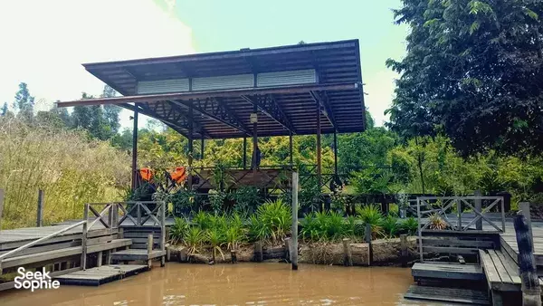 Muddy riverbank at a jungle eco-lodge with a raised wooden jetty and canopy for boats on the Kinabatangan River