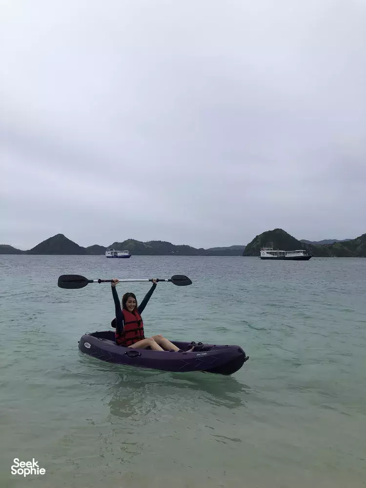 Kayak on calm sea during a join-in Komodo boat trip off the coast, with boats and hills in view — Labuan Bajo