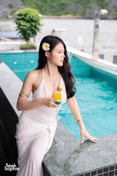 Woman holding a cocktail beside the infinity-style pool on a luxe Cat Ba cruise, wearing a white dress with hair flower