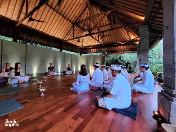 Participants seated cross-legged in a peaceful indoor pavilion, guided through a Balinese blessing ceremony within Canggu