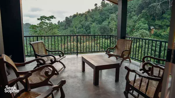 Covered lodge balcony with seating looking out over green tea-covered hills at Old Frankland Tea Estate in Kandy
