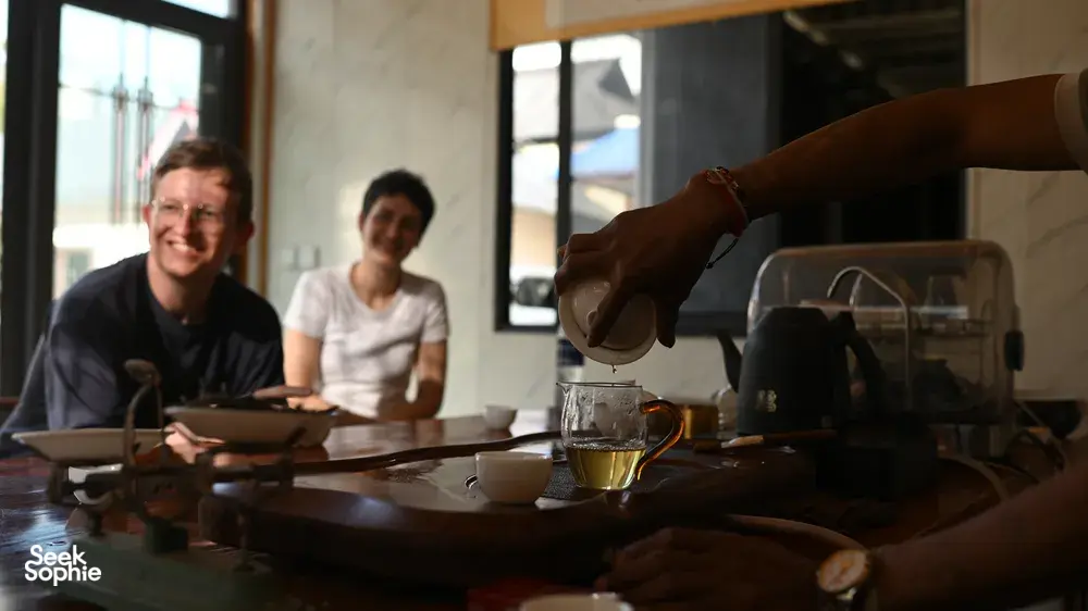 Detik merasa teh ketika pemandu tempatan menuangkan teh untuk kumpulan kecil di meja dalam pengalaman teh 3H2M di Xishuangbanna