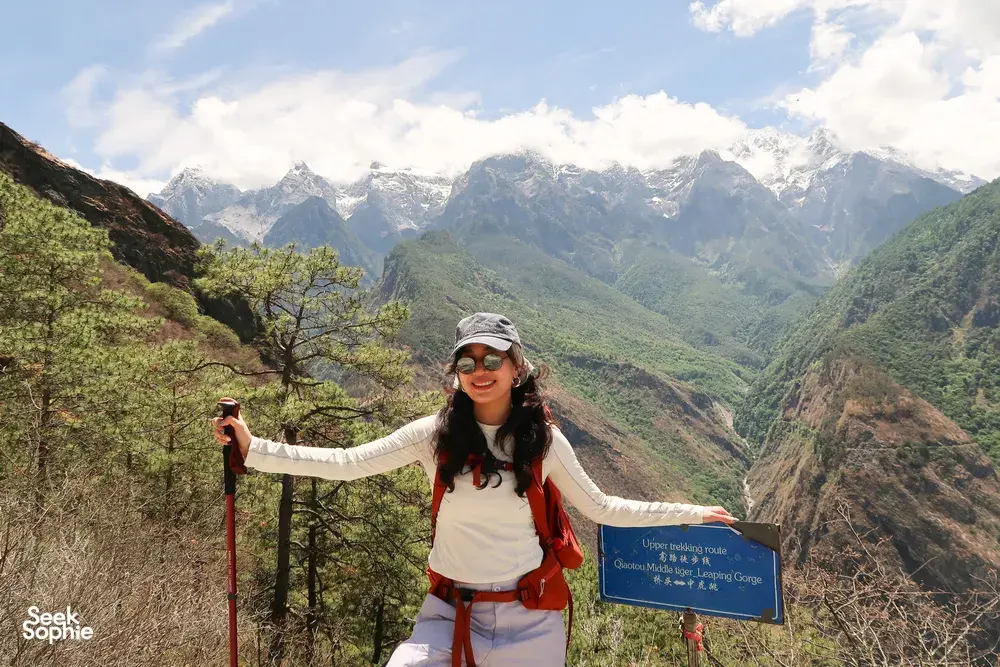 Backpack hiker smiling by a trail sign at a mountain lookout over Tiger Leaping Gorge in Lijiang during the 2D1N high trail
