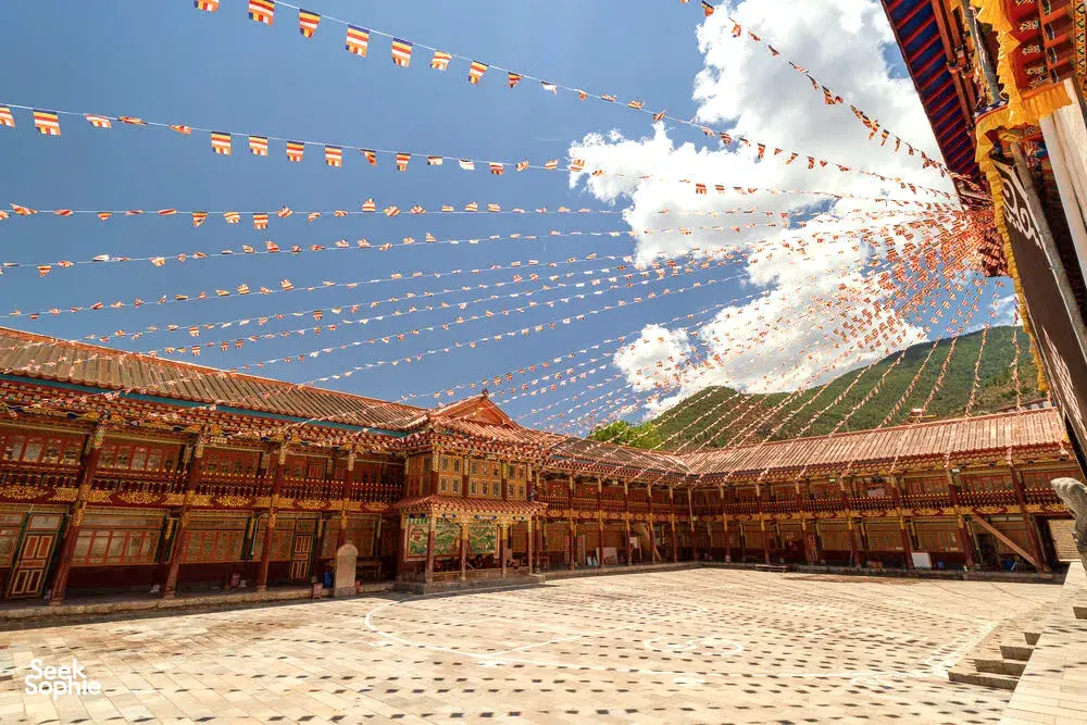 Prayer flags strung over a traditional Tibetan courtyard, with ornate wooden corridors and blue sky at Shangri-La