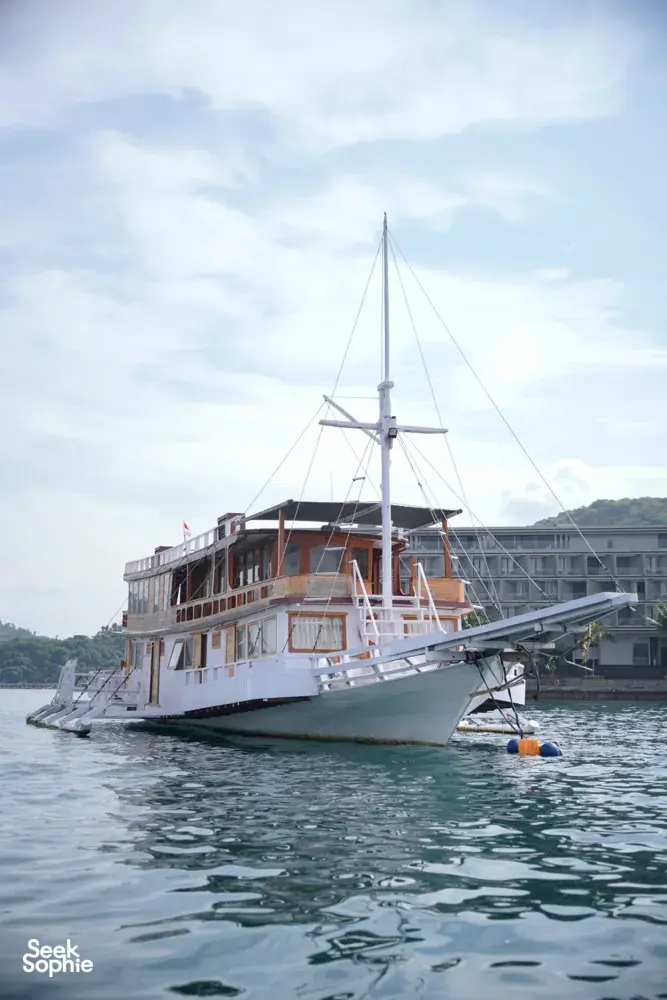 Wooden liveaboard sailing boat with rigging moored on calm water for a 3D2N join-in Komodo trip in Labuan Bajo