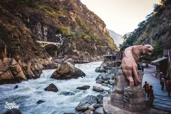 Stone elephant statue beside a walkway, overlooking a dramatic gorge with rushing river water and towering cliffs in Northern Yunnan