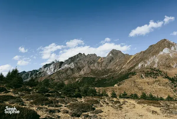 Jade Dragon Snow Mountain ridgeline near Lijiang under a blue sky, with rocky slopes and scattered evergreen trees