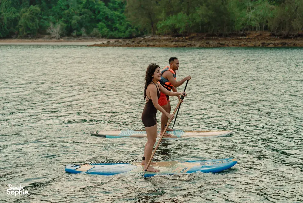 Travellers paddleboarding on calm water near a green shoreline from a Kota Kinabalu area sea cruise