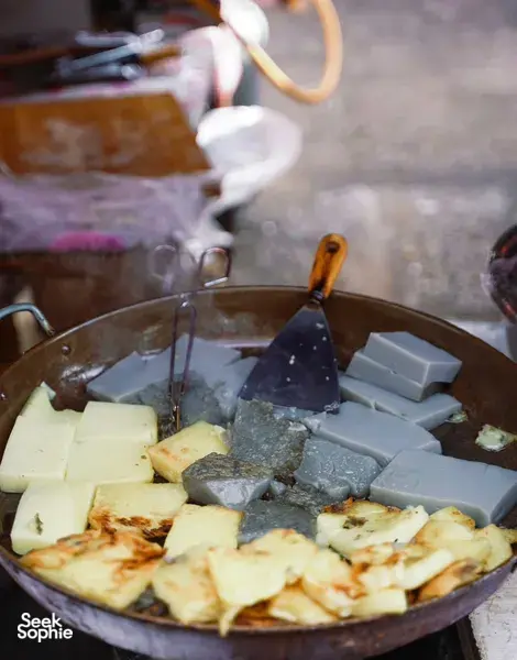 Smoky street-food wok in Lijiang with cubed foods sizzling over charcoal at a street stall during a local food hunt