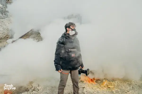 Traveller in a protective mask standing in thick sulphur fumes above the crater during a guided 5D4N Ijen stop at Mt Ijen