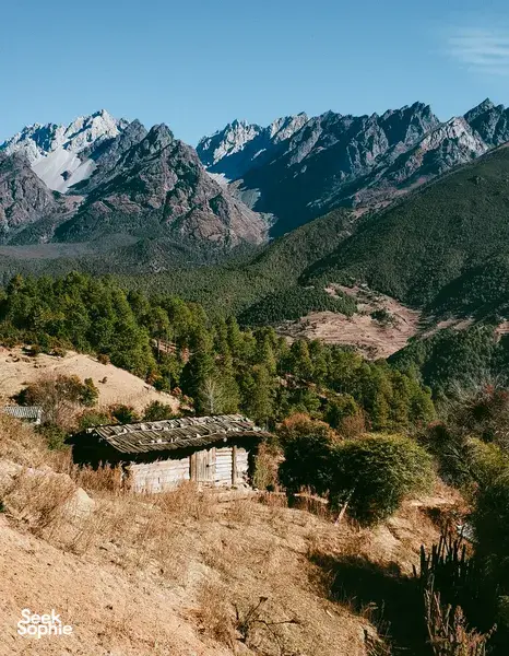 Rugged village hut overlooking pine valley and snowcapped peaks on the way to Wenhai Wetlands from Lijiang