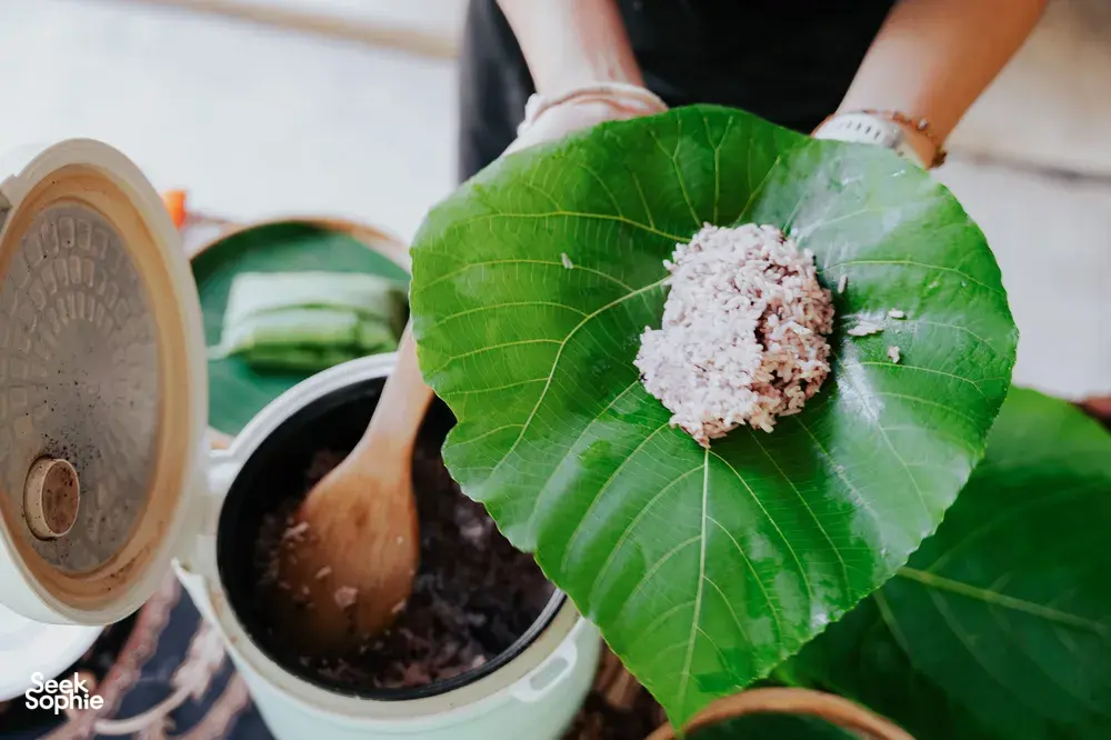 Hands preparing Indigenous Sabahan ingredients in Kota Kinabalu, holding a large leaf with a paste over a pot