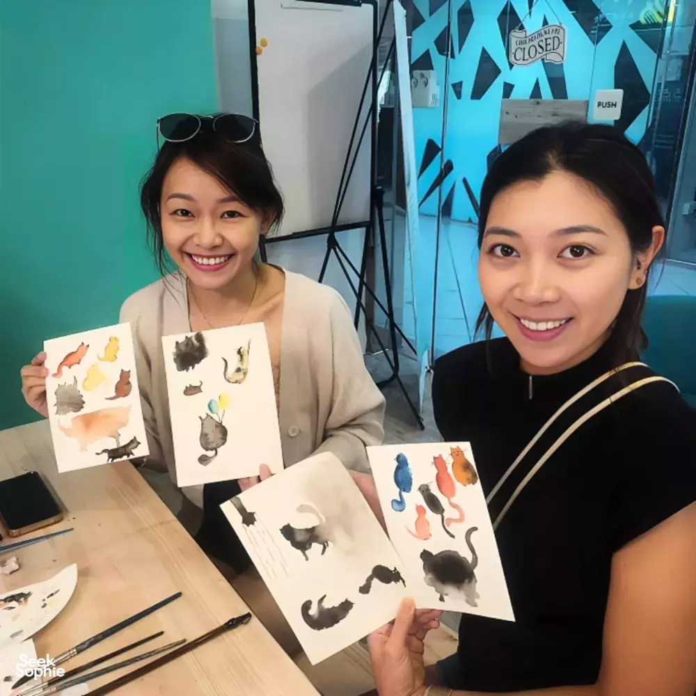 Art For Good art therapy in Singapore: two women seated at a craft table showing pet-themed cards during workshops in Singapore