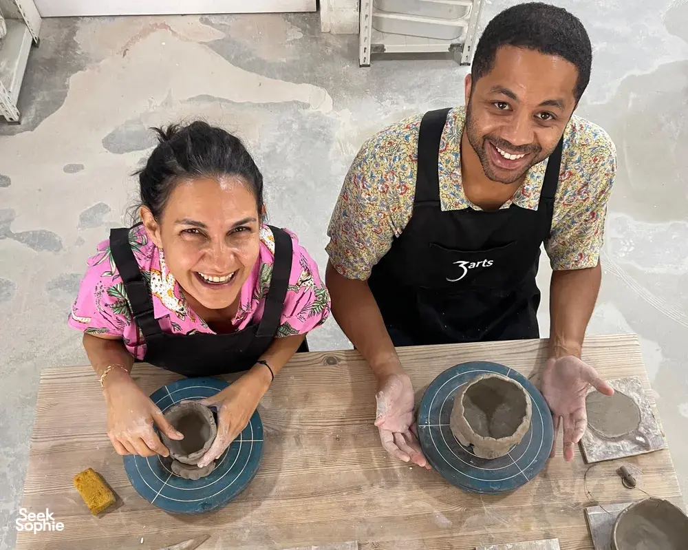 Tuan rumah 3Arts Pottery tersenyum sambil membuat mangkuk tanah liat dengan tangan di atas roda putar dalam lokakarya studio di Singapura