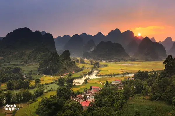 Sunset over Cao Bang valley with patchwork rice fields, a winding river, and dark limestone karst mountains in the distance