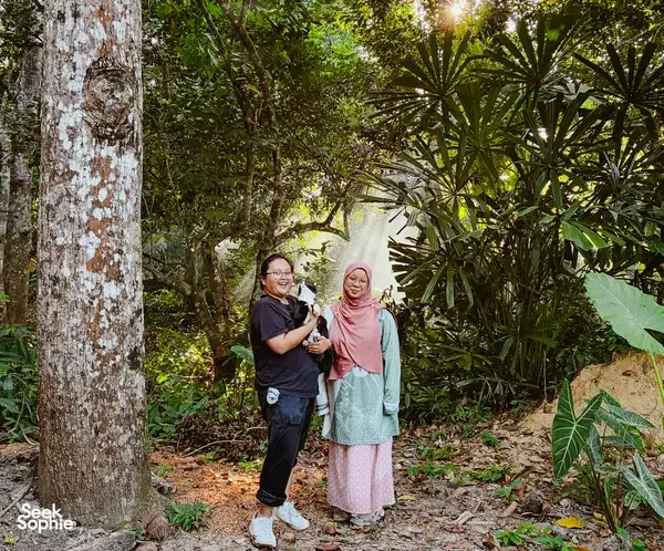 Two travellers standing in a shaded garden at Kebun Lidstari in Langkawi, surrounded by palms and dense tropical greenery