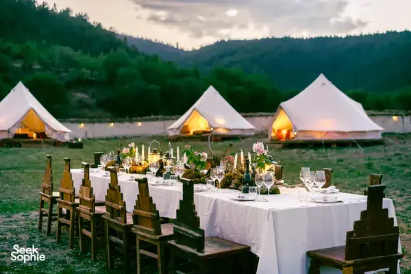 Shangri-La mountain valley camp dinner with set dining table in front of lit white tents at dusk, Mission Liotard stay