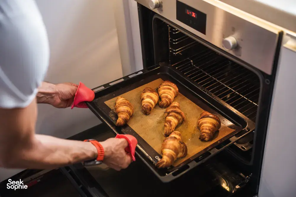 Hands in red oven gloves sliding a tray of croissants out of the oven at French Cooking Lab in Singapore