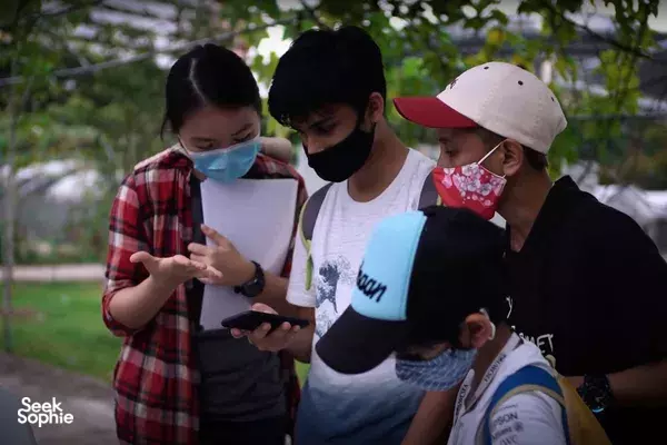 Masked participants compare hunt clues on paper and phones during an outdoor sustainability scavenger hunt in Singapore