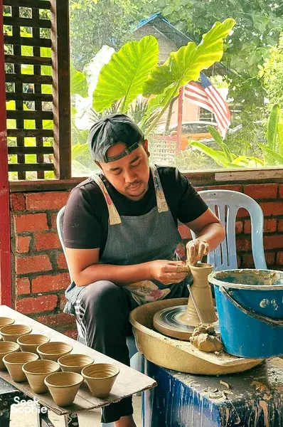 Ilham Ceramic artisan in Langkawi wheel-throws and trims a small pot while working at a clay-lined table
