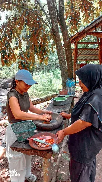Former-logger forest walk cooking in Lombok: two people prep ingredients at a stone mortar table in the shade
