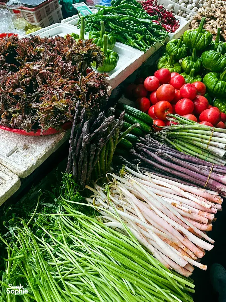 Lijiang market stall piled with seasonal greens, chillies and tomatoes for a Yunnan cooking day, ready for the morning market walk
