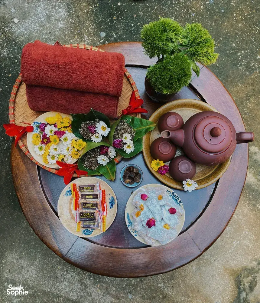 Top-down view of a round tray tea spread near Hanoi: purple teapot with cups, flowers, and greenery for a herbal brew