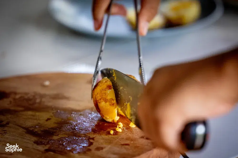 Close-up of a cook turning food with metal tongs on a wooden prep board during a Mae Kampong forage-to-table cooking class, Chiang Mai