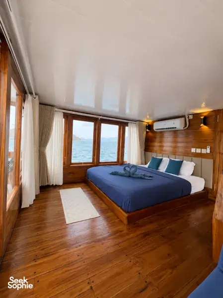 Blue-dressed beds in a wooden cabin with sea-facing windows on board the 3D2N shared Komodo cruise, Komodo Island