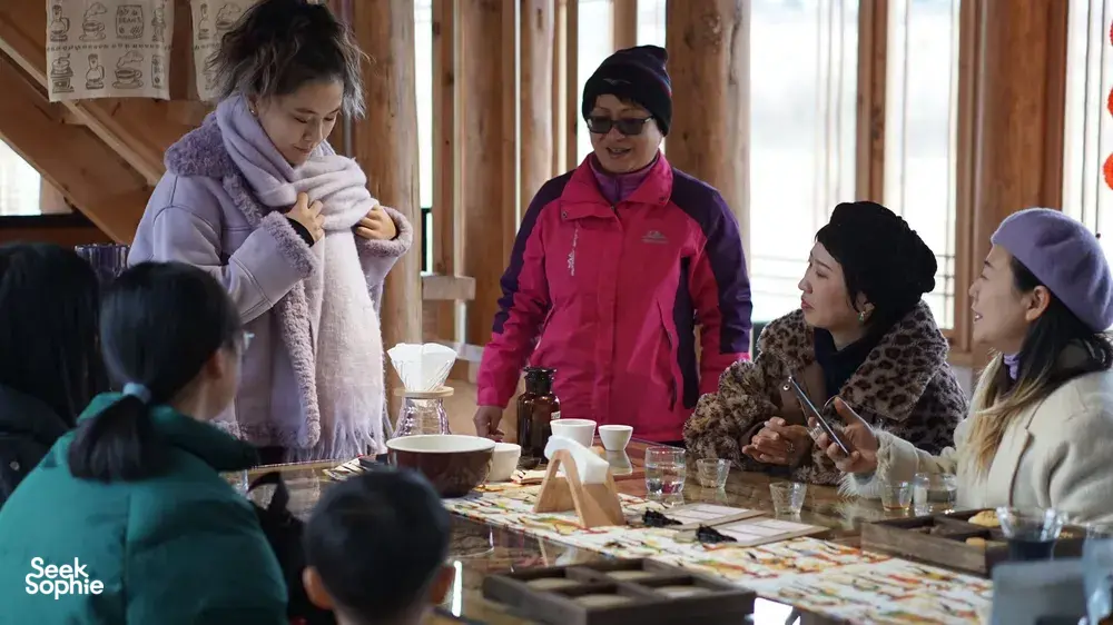 Family-run coffee tasting in Lijiang: host in a red jacket and guests sit around a long table with cups, drippers and filters