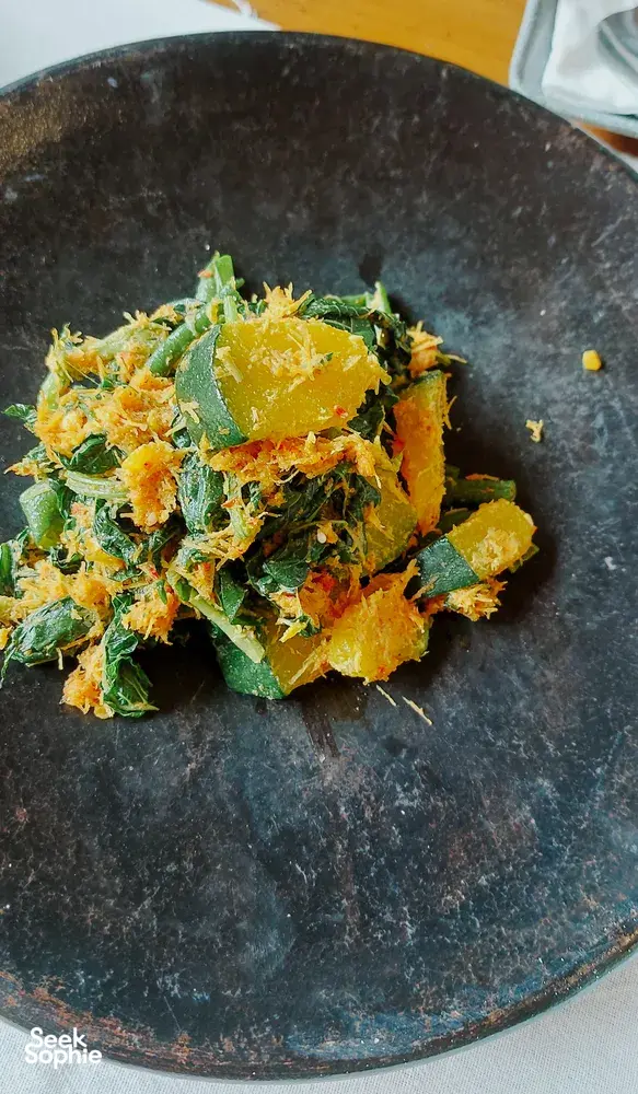 Green and golden shredded vegan topping on a dark plate, prepared in a Traditional Manggarai vegan cooking class in Labuan Bajo