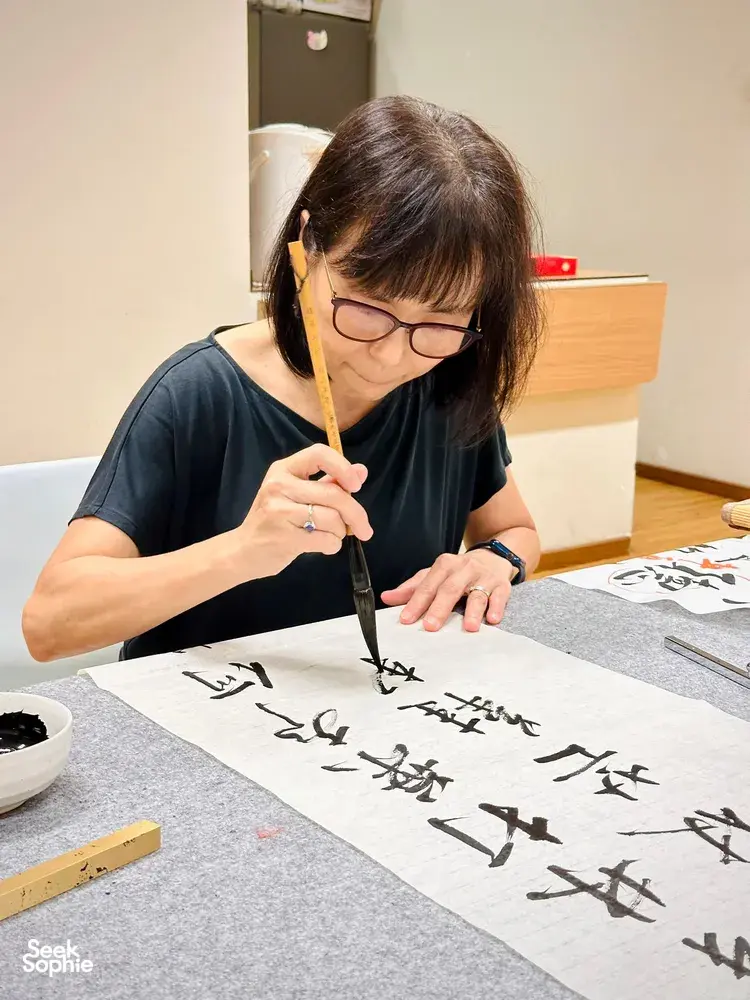 Singapore Chinese calligraphy lesson with a woman writing black characters in ink strokes on rice paper with a brush