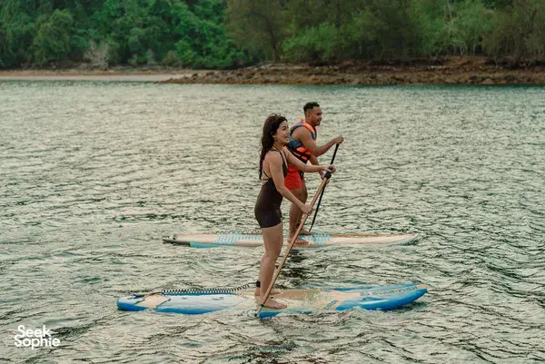 Travellers paddleboarding on calm water near a green shoreline from a Kota Kinabalu area sea cruise