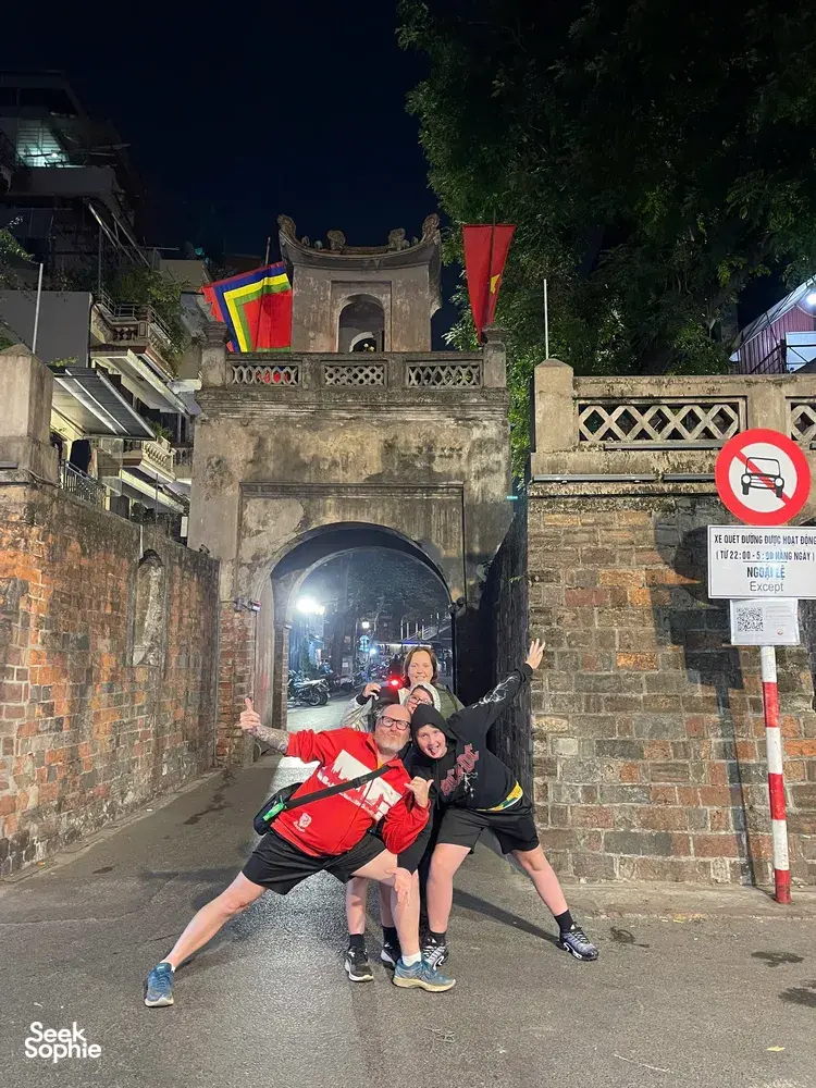 Travellers posing in a narrow illuminated laneway beneath an old stone arch during a Hanoi night food experience
