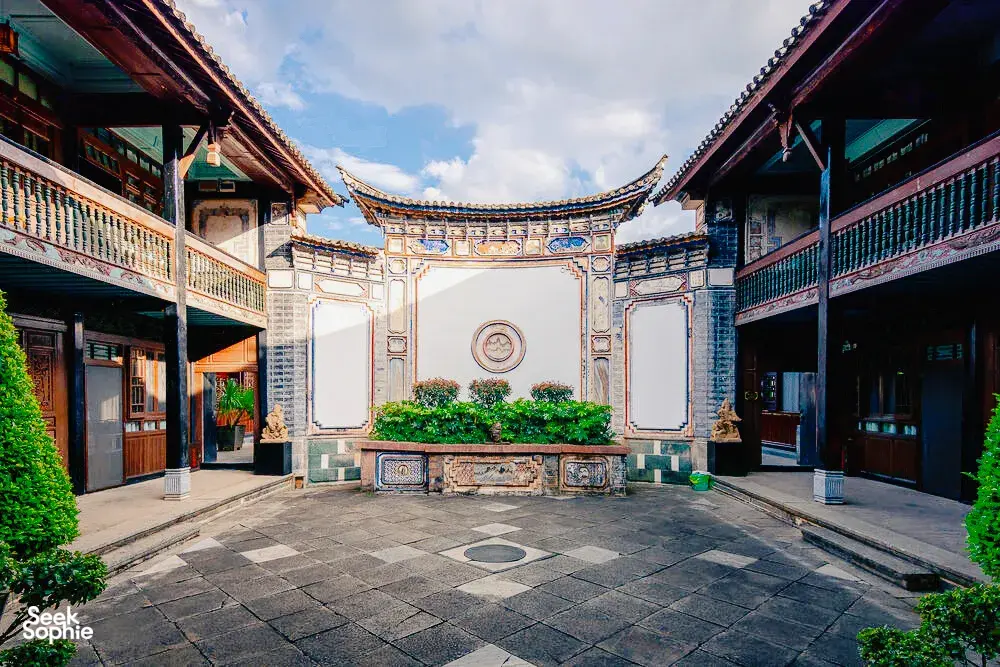 Pintu gerbang laman tradisional Bai di Linden Centre, Pekan Lama Xizhou, Dali, membingkai patio batu dan perincian ukiran biru-putih
