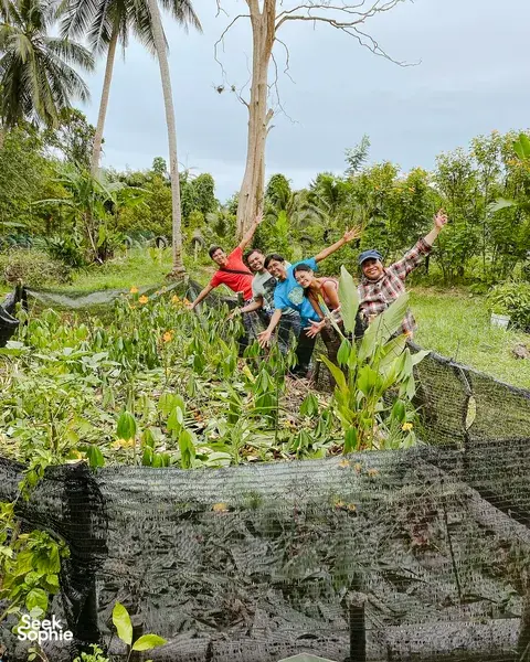 Travellers posing in the greenery of Kebun Lidstari permaculture farmstay, Langkawi, with raised garden beds and palms nearby