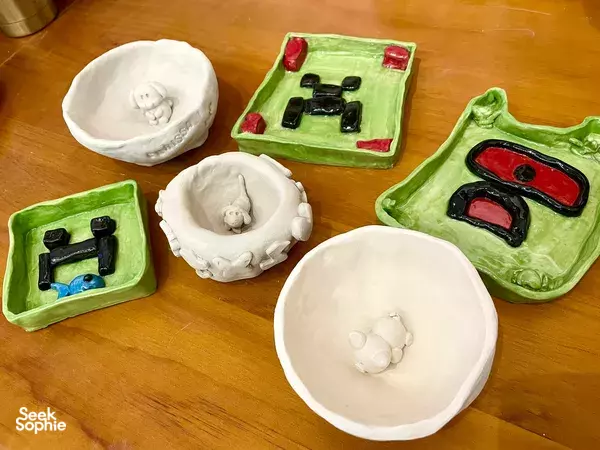 Finished ceramic bowls and trays from a kids pottery class in Singapore on a wooden table, glazed and painted — workshops in Singapore