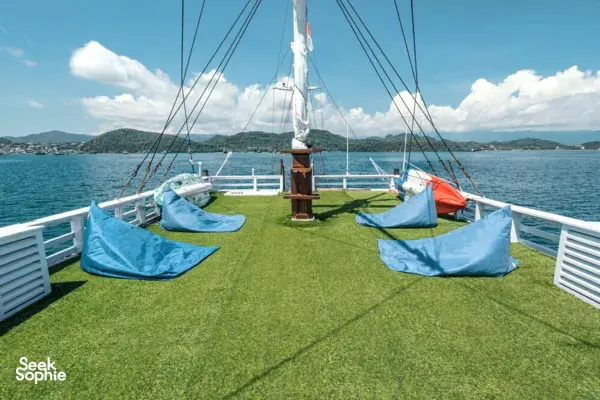 Private 3D2N Komodo cruise on a sleek white phinisi: green sun deck with blue lounging cushions and sail rigging in Labuan Bajo