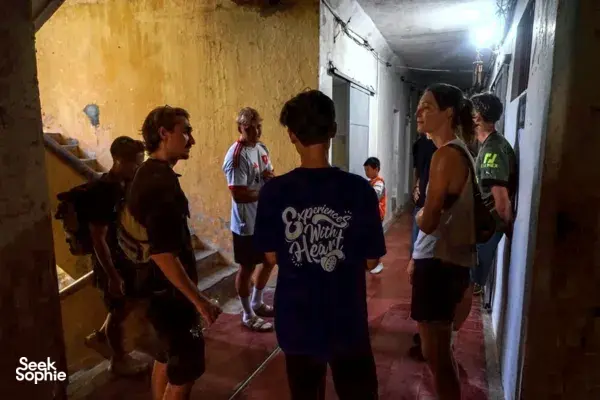 Tour group walking through a dim corridor in Hanoi's hidden wartime passage, with backpacks and headsets facing forward